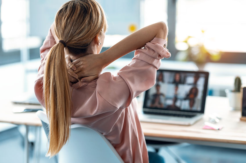 Back view of female employee taking a break one moment while speaking on video call with diverse colleagues on online briefing with laptop at home.