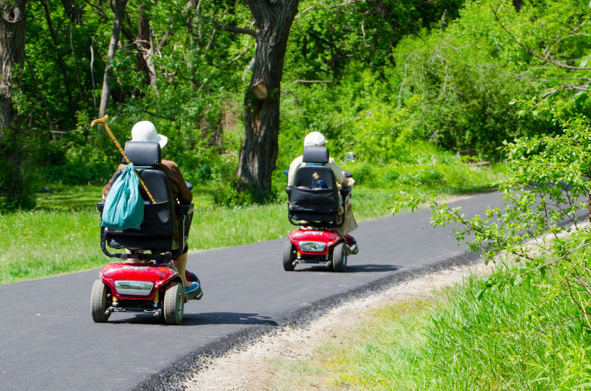 Couple riding mobility scooters on paved path